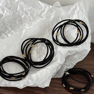 Detail of high elasticity black hair ties featuring minimalist gold metal cylinder joints