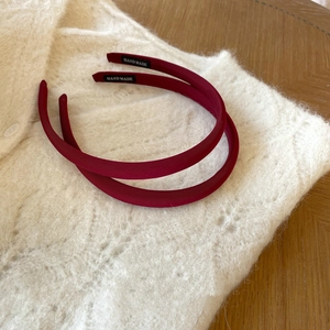 Détail de deux serre-têtes en satin rouge vin avec étiquette Hand Made sur tricot