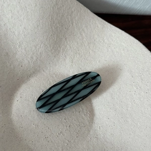 Detail of acetate oval hair clip with blue-grey plaid pattern and France Handmade text
