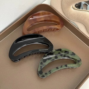 Three acetate hollow crescent hair claws in amber, black, and marble green displayed on a tray