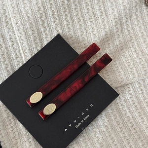 Detail view of two dark red marble acetate hair clips with gold oval logo on tweed