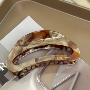 Detail of tortoiseshell acetate claw clip with golden logo and crescent hollow design