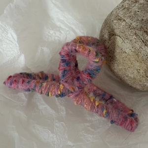 Dettaglio di un grande fermaglio per capelli in lana intrecciata rosa con accenti colorati