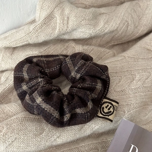 Detail of a dark brown plaid oversized scrunchie with a smiling face label on wool fabric