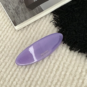 Detail of light purple acetate hair clip with gold lettering on white fabric