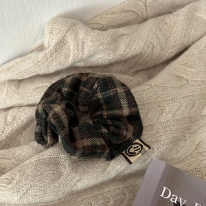 Close-up of dark plaid scrunchie with brand label on a cozy knitted sweater background
