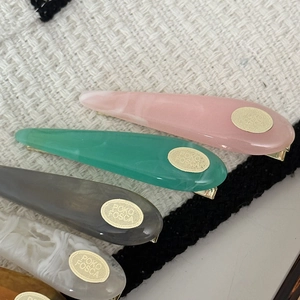 Water-drop acetate hair clips in multiple colors with gold metal logo accents