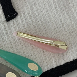 Detailed close-up of teardrop acetate hair clips in pink, green, and grey with gold base