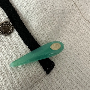 Detailed close-up of emerald green teardrop hair clip with a gold metallic oval logo label