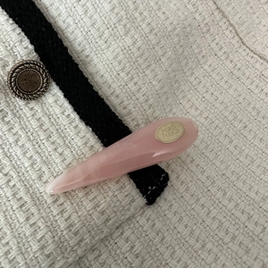Detailed view of pink acetate hair clip on beige tweed fabric with gold logo tag