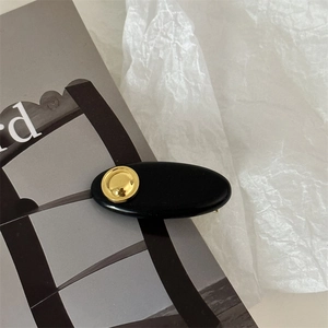 Macro shot of minimalist black oval resin hair clip with gold metal circular accent