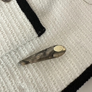 Detail view of water-drop acetate hair clip with gray marble texture and gold logo