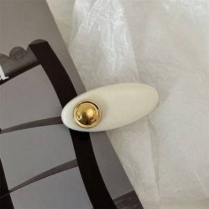 Close-up of a cream acrylic hair clip with a gold metal center on a magazine background
