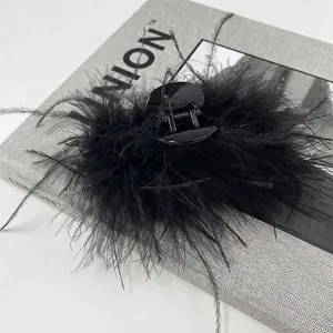 Detail view of a large black ostrich feather hair claw clip on a textured fabric surface