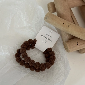 Detail view of two brown textured plush hair ties on a minimalist heart display card