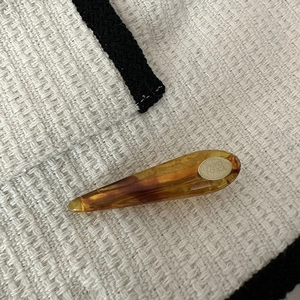 Macro shot of tortoiseshell acetate hair clip with an oval gold brand logo on tweed