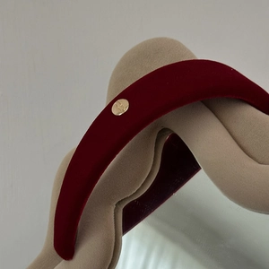 Detailed close-up of burgundy velvet headband with gold logo on a beige wavy mirror