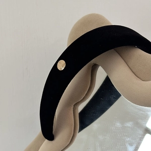Close-up of black velvet headband featuring a circular gold metal logo detail