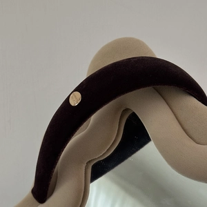Detailed macro shot of deep brown velvet headband with circular golden metal brand logo