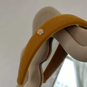 Close-up of mustard yellow velvet padded headband with a gold metal logo detail