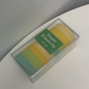 Close-up of candy-colored elastic hair ties in a transparent storage box with green card