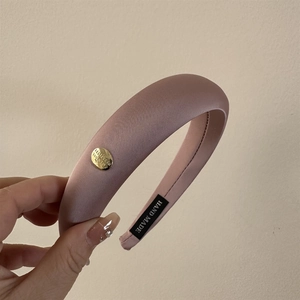 Détail d'un serre-tête en satin rose avec boucle dorée et étiquette artisanale