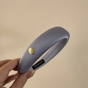 Détail d'un serre-tête en satin bleu clair avec bouton doré et étiquette faite à la main