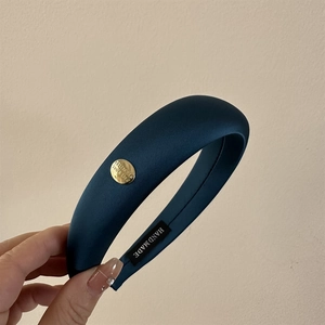 Détail d'un serre-tête en satin bleu marine avec boucle dorée et étiquette artisanale