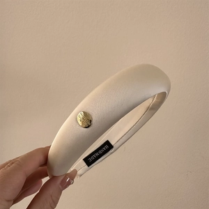 Détail d'un serre-tête en satin crème avec boucle dorée et doublure antidérapante
