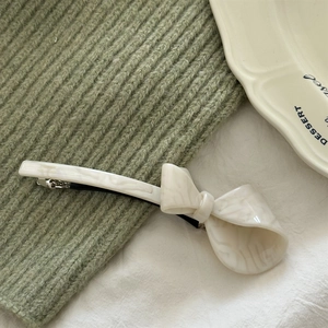 Close-up of cream marble textured acetate bow hair clip on a white ceramic plate