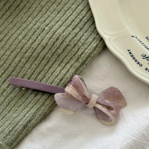 Detailed close-up of acetate bow hair clip with purple marble pattern on knit fabric