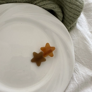 Macro shot of star-shaped acetate hair clips in brown and amber on white ceramic