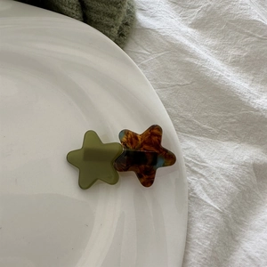 Star-shaped hair clips in olive green and amber tortoiseshell on a white ceramic plate