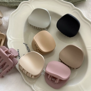 Close-up of matte medium hair claw clips in assorted Morandi colors on a white ceramic plate