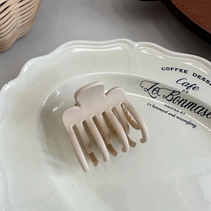 Detailed view of matte beige hair claw clip on a white ceramic tray with natural lighting