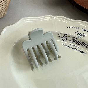 Macro detail of the matte greyish blue shark hair claw clip in a minimalist cream tray