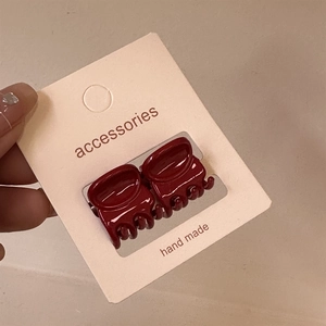 Gros plan de deux mini-pinces à cheveux rouge bordeaux sur une carte cadeau
