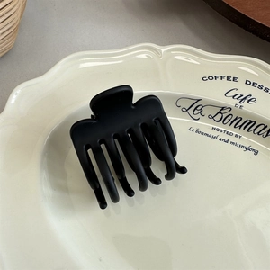 Close-up of a matte black medium hair claw clip on a decorative ceramic dish