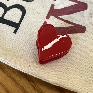Gros plan d'une mini pince à cheveux rouge brillante en forme de cœur sur toile blanche