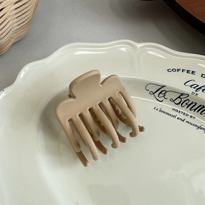 Detail view of a matte khaki hair claw clip placed on a vintage decorative white plate