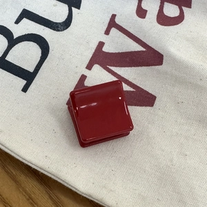 Détail d'une mini pince à cheveux carrée rouge foncé en résine brillante sur toile