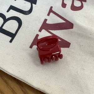 Détail d'une mini pince à cheveux bordeaux brillante sur un fond de sac en toile