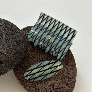 Translucent blue hair clip set with black geometric pattern on volcanic stone background