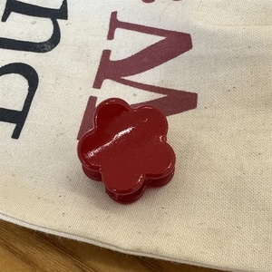Détail macro d'une mini pince à cheveux en forme de fleur rouge sur un tissu beige doux