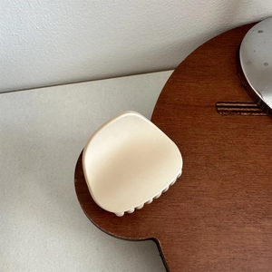 Macro shot of matte beige medium hair claw clip on wooden desk highlighting frosted texture