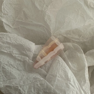 Close-up of pink and amber marble resin duckbill hair clip on white paper background