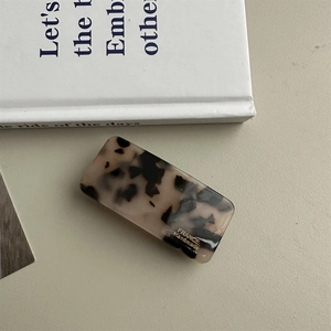 Macro shot of handmade tortoiseshell barrette with gold logo on a minimalist background