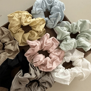 Set of eight colorful fabric scrunchies in varied pastel tones displayed on a wooden tray