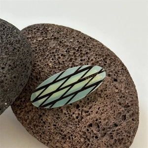 Detail of light green acetate oval hair clip with black grid and France Handmade text