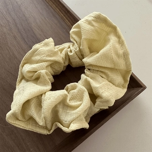 Detail of light yellow textured scrunchie on dark wooden tray with elegant fabric texture
